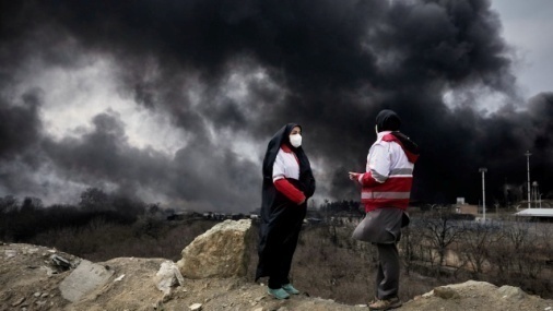 Two people stand in front of black smoke