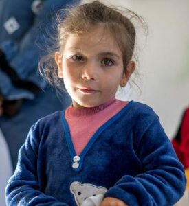 Young girl holds a white bag with UNICEF and Aiera logos, receiving winter clothes and school kits.
